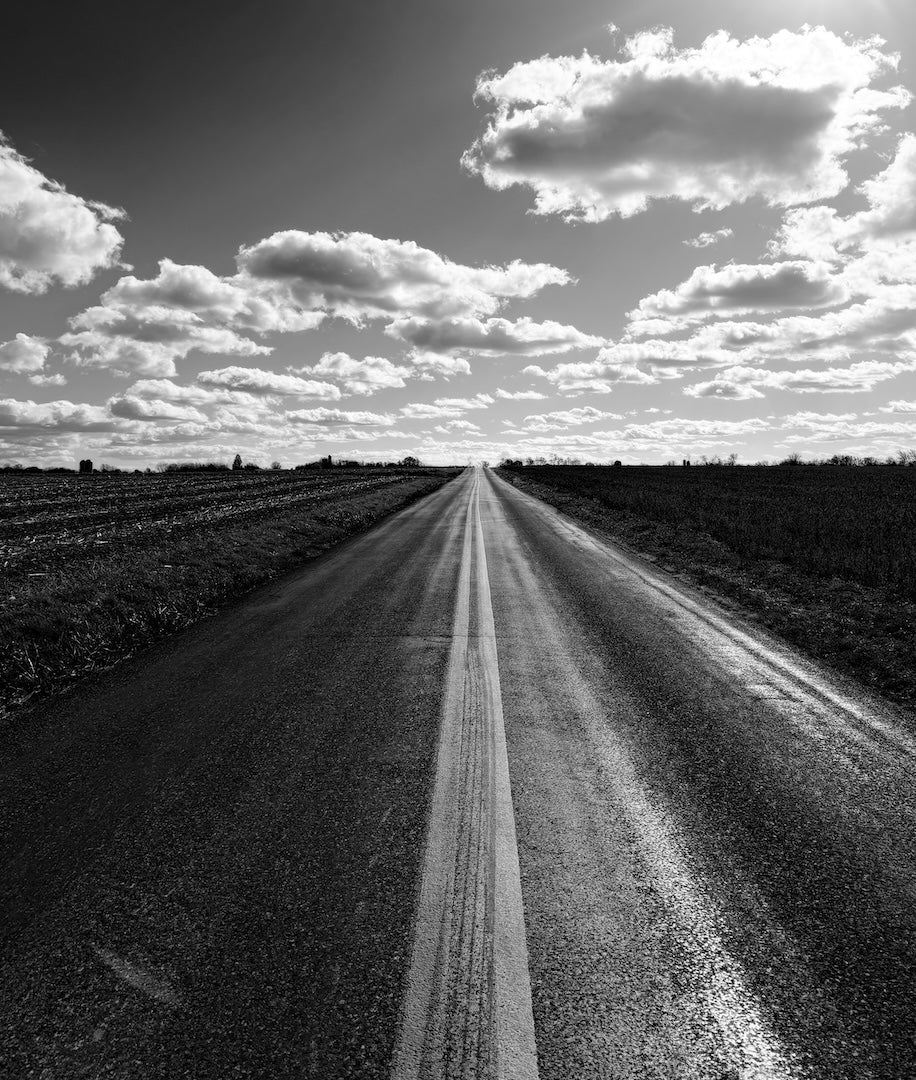 Winding dirt road through a field with a cloudy sky above.